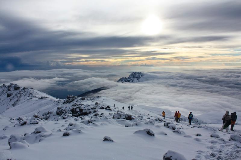 Climbers crossing snow near Stella Point at sunrise, high above a sea of clouds