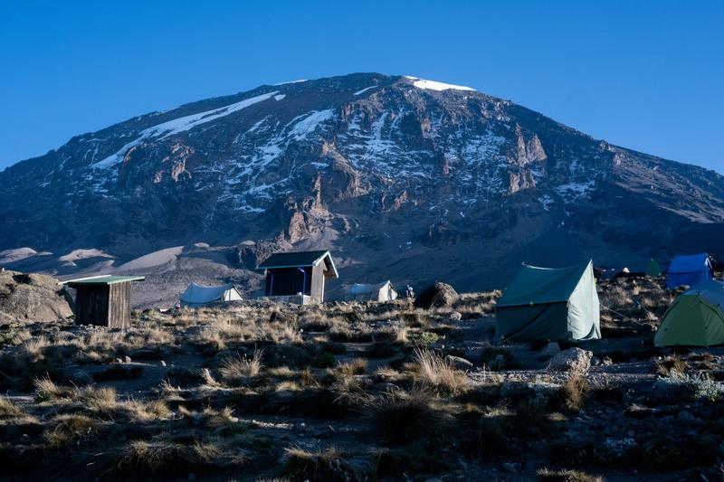 Tents and huts of a campsite on Kilimanjaro, with the snow-streaked slopes of Kibo behind